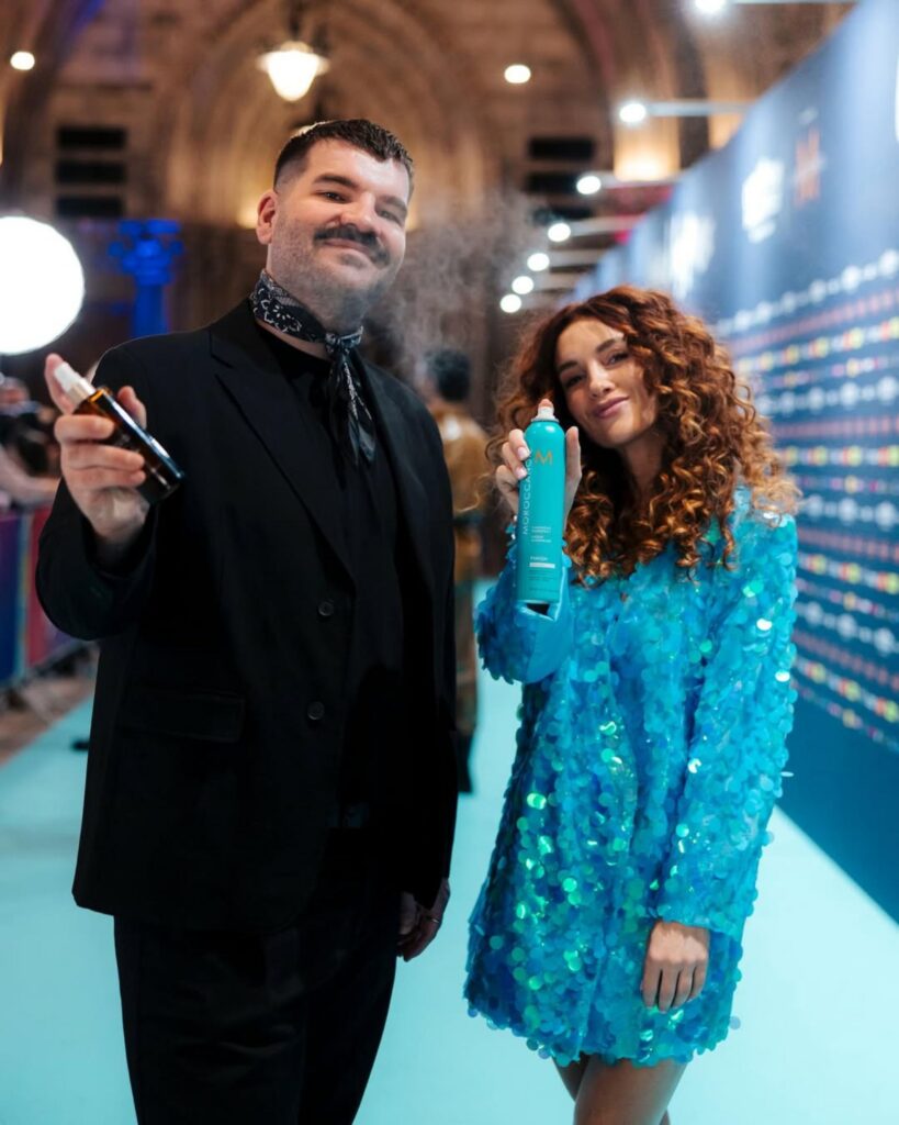 Two hairstylists holding Moroccanoil products on a turquoise carpet at Eurovision