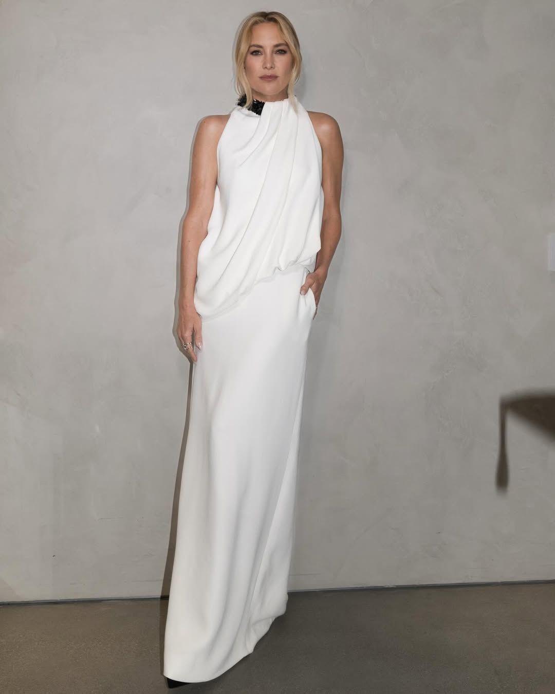 Full-length view of Kate Hudson in a white gown paired with a sleek, modern French twist updo