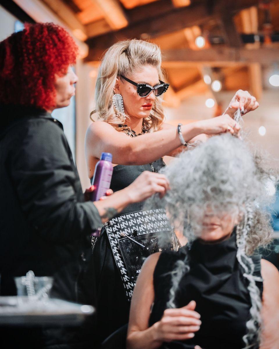Ashlee Norman styles a model’s textured gray hair onstage while holding a Bumble and bumble product during a live education demonstration.