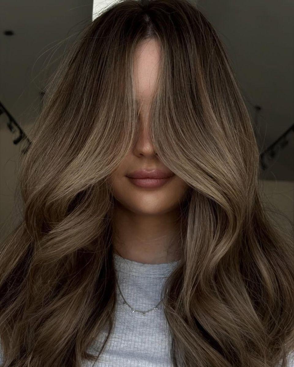 Long dimensional bronde hair with soft waves, a center part and bright face-framing blonde highlights.