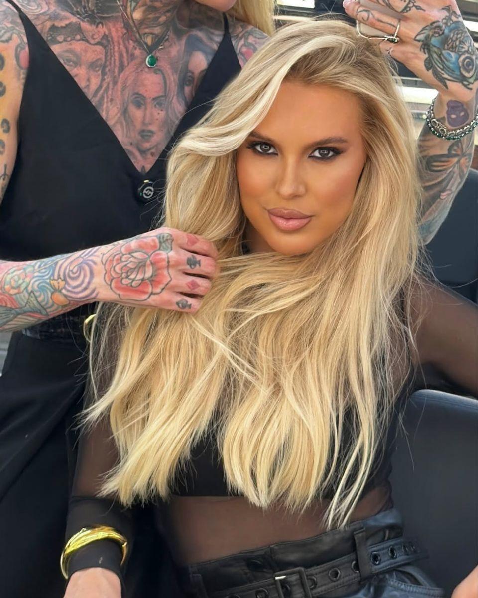 Portrait of long champagne blonde hair with soft beige dimension, a seamless root blend and polished waves styled over a sheer black top.