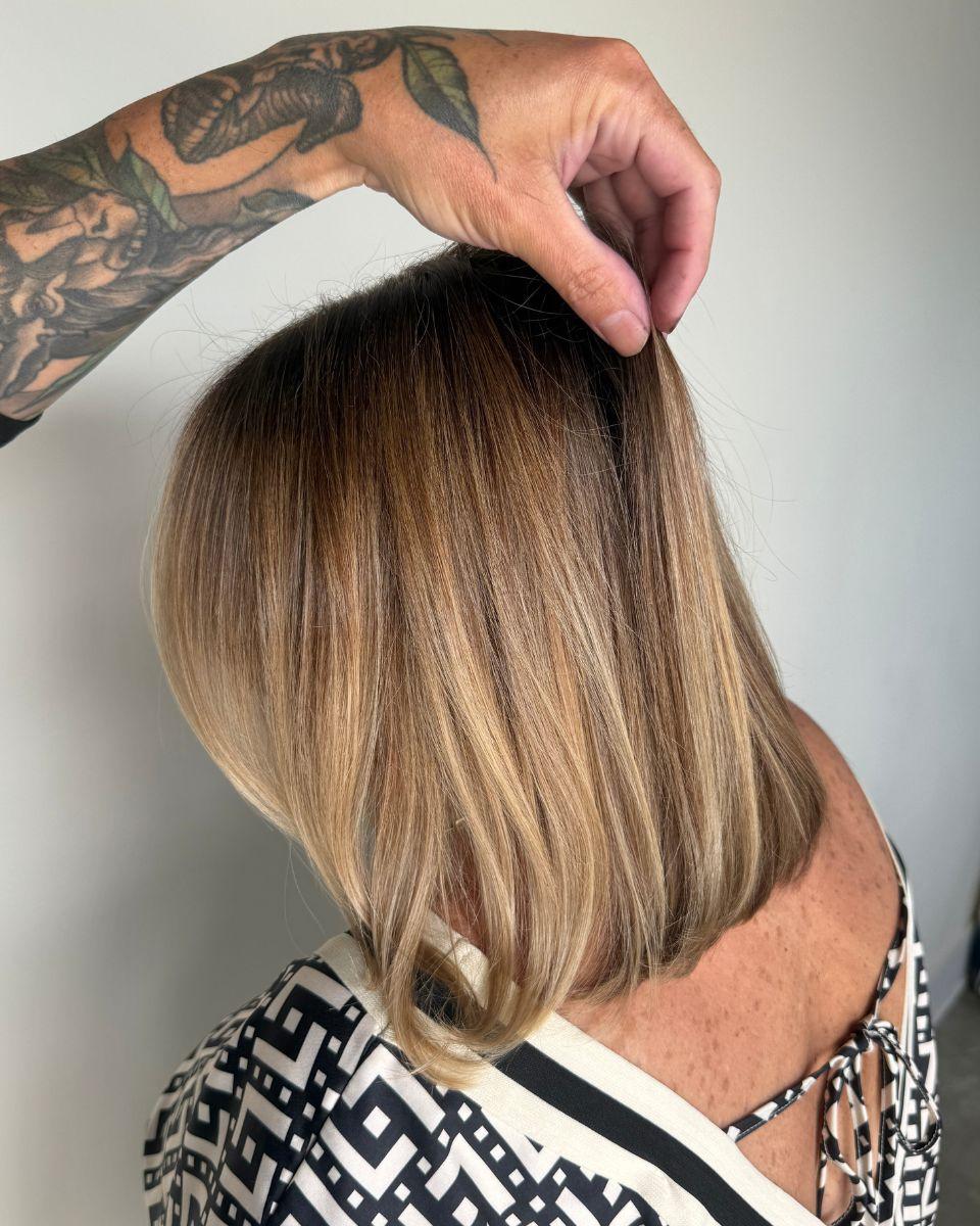 Mickey lifts a section of the finished blonde hair to show the blended root coverage and dimensional color result.