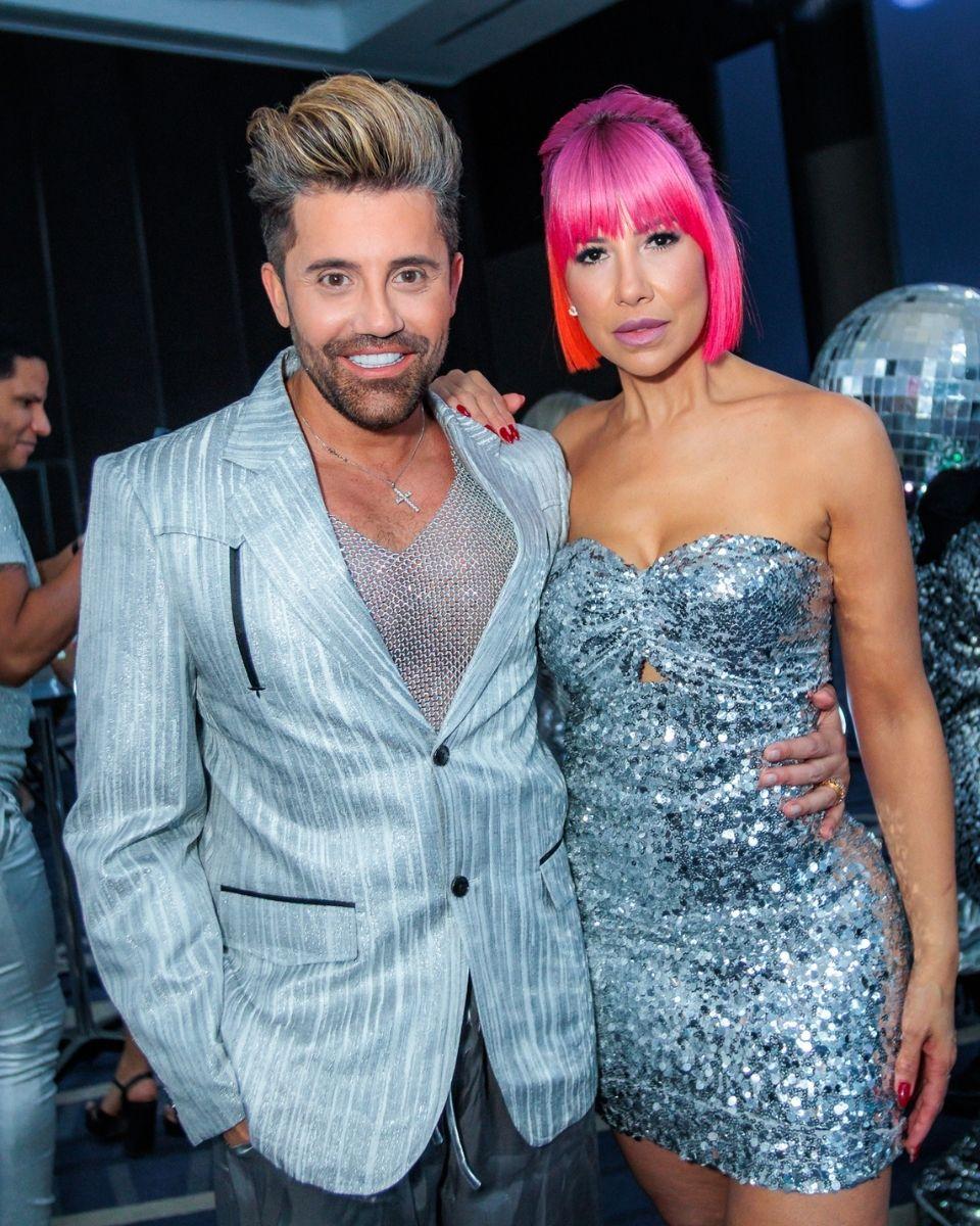 Gabriel Samra and Lisa Hernandez pose together in silver outfits during a TRUSS Professional event party.