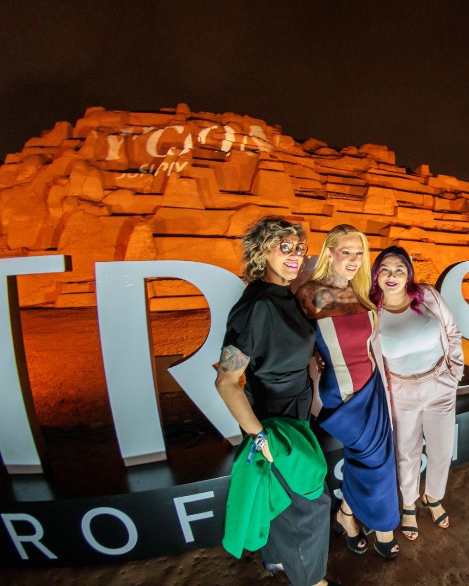 Guests pose with Ambassador Melissa Schlukebier in front of an illuminated TRUSS sign and ancient ruins during an outdoor evening party in Lima, Peru.