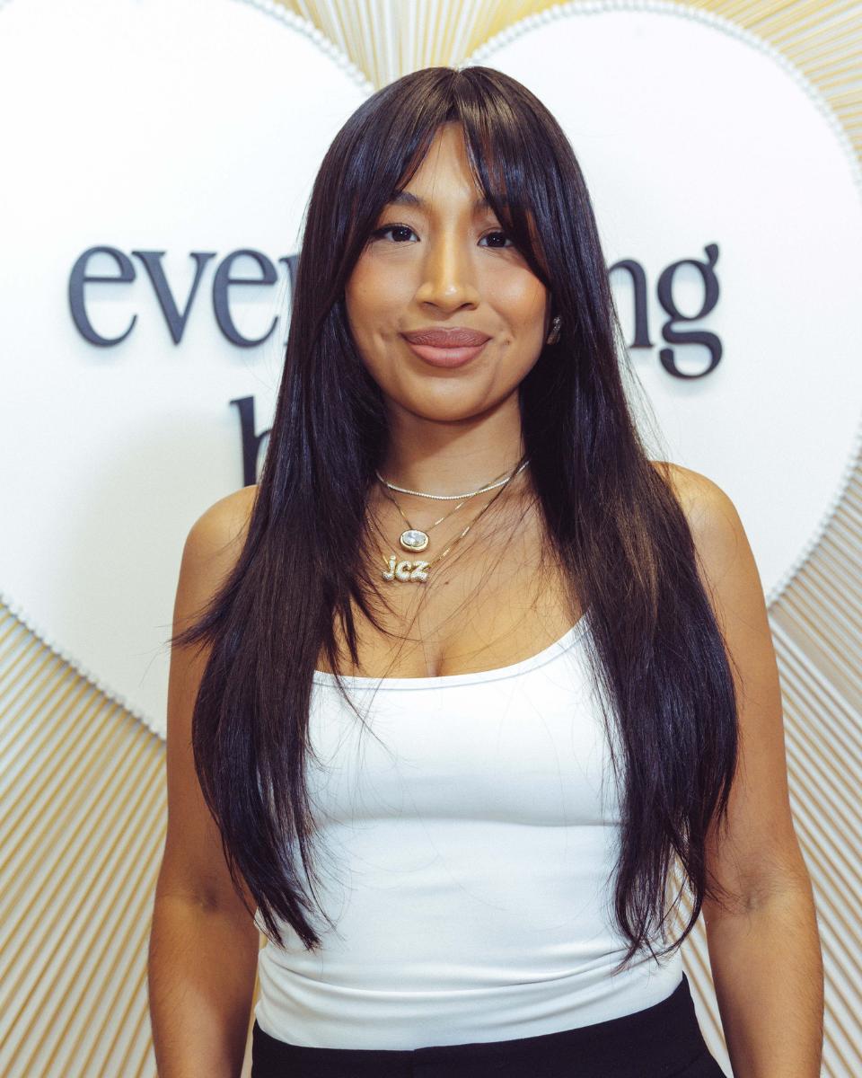 A guest poses in front of the Everlasting Bonds backdrop with long, shiny dark hair after her treatment.