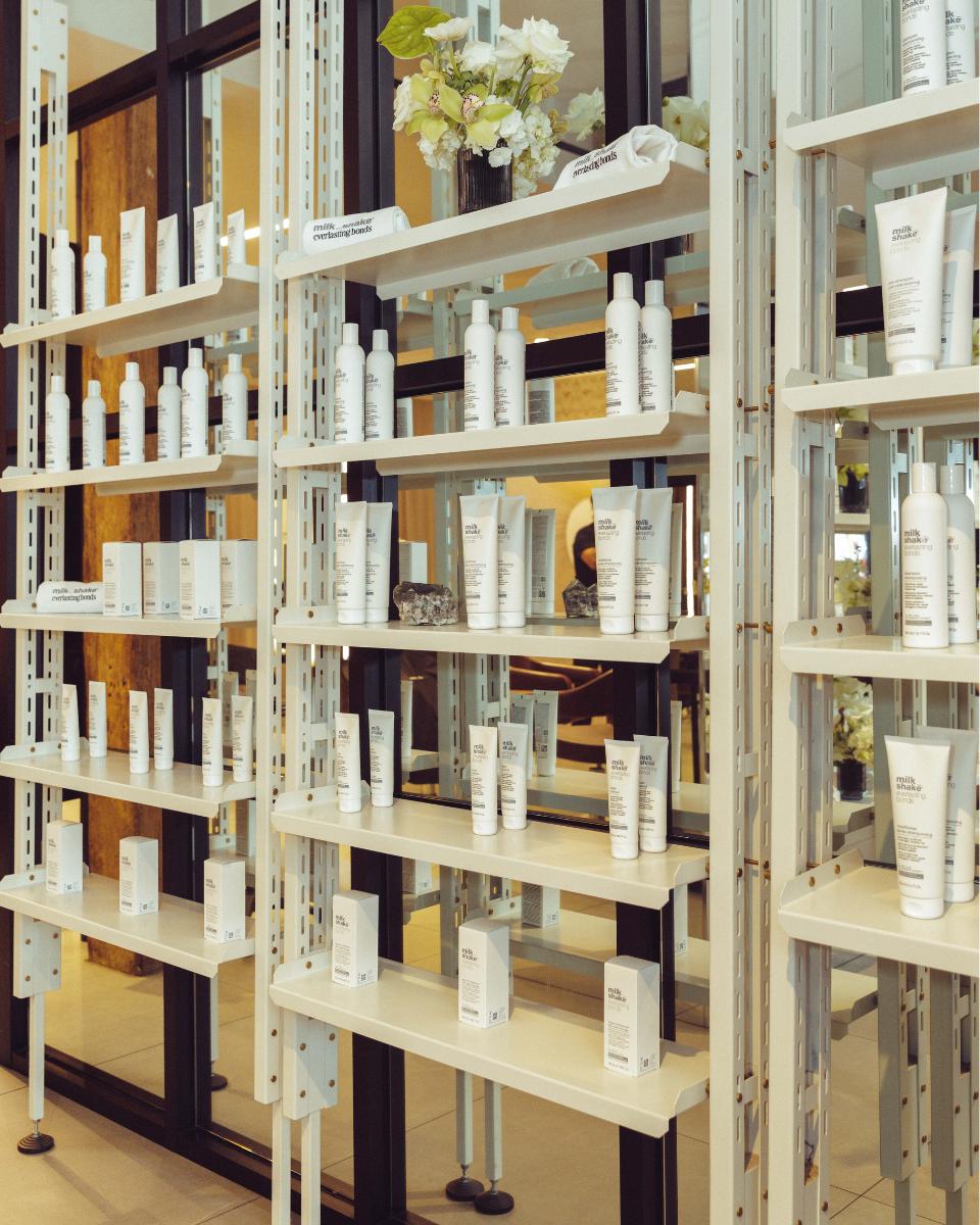 milk_shake Everlasting Bonds products are displayed on white salon shelves with florals and branded accessories.