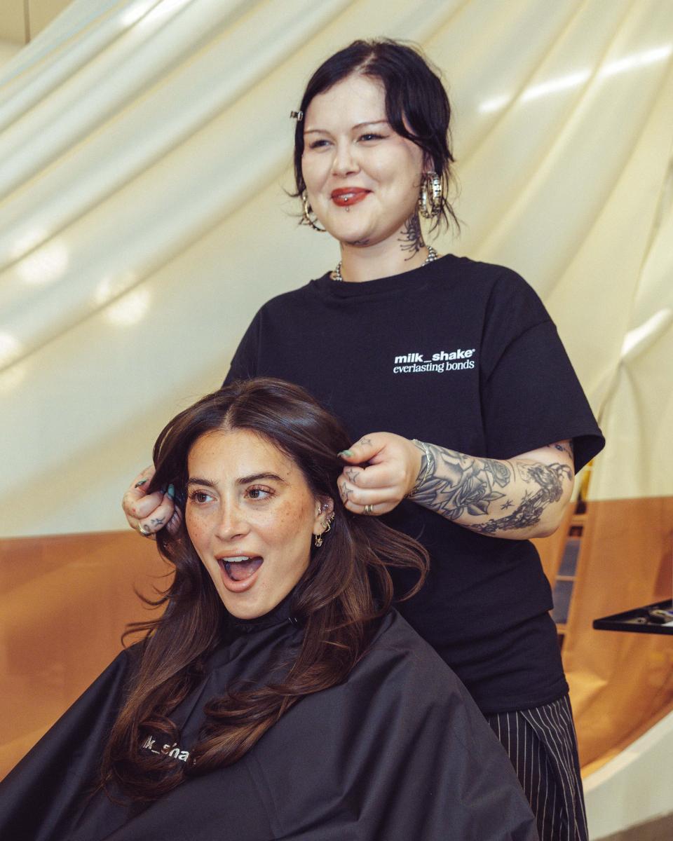 A guest reacts to her finished brunette style while a milk_shake stylist stands behind her at the launch event.