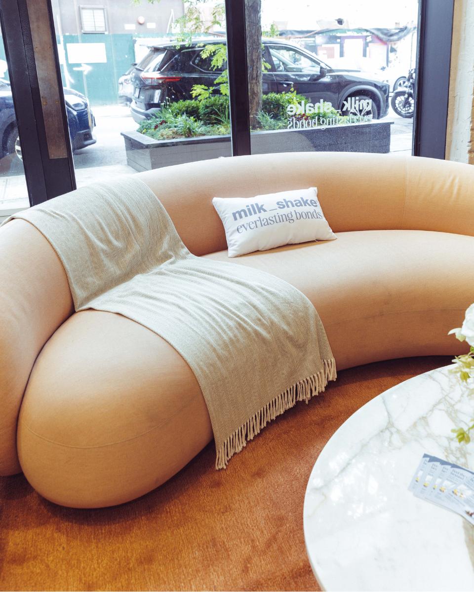 A branded milk_shake Everlasting Bonds pillow sits on a curved sofa inside Rob Peters Salon.