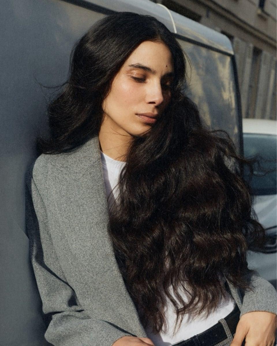 Model with long, dark, softly waved hair wearing a gray blazer outdoors, showing the power of Perfect Hair Day Sheer Clean Dry Shampoo Mist
