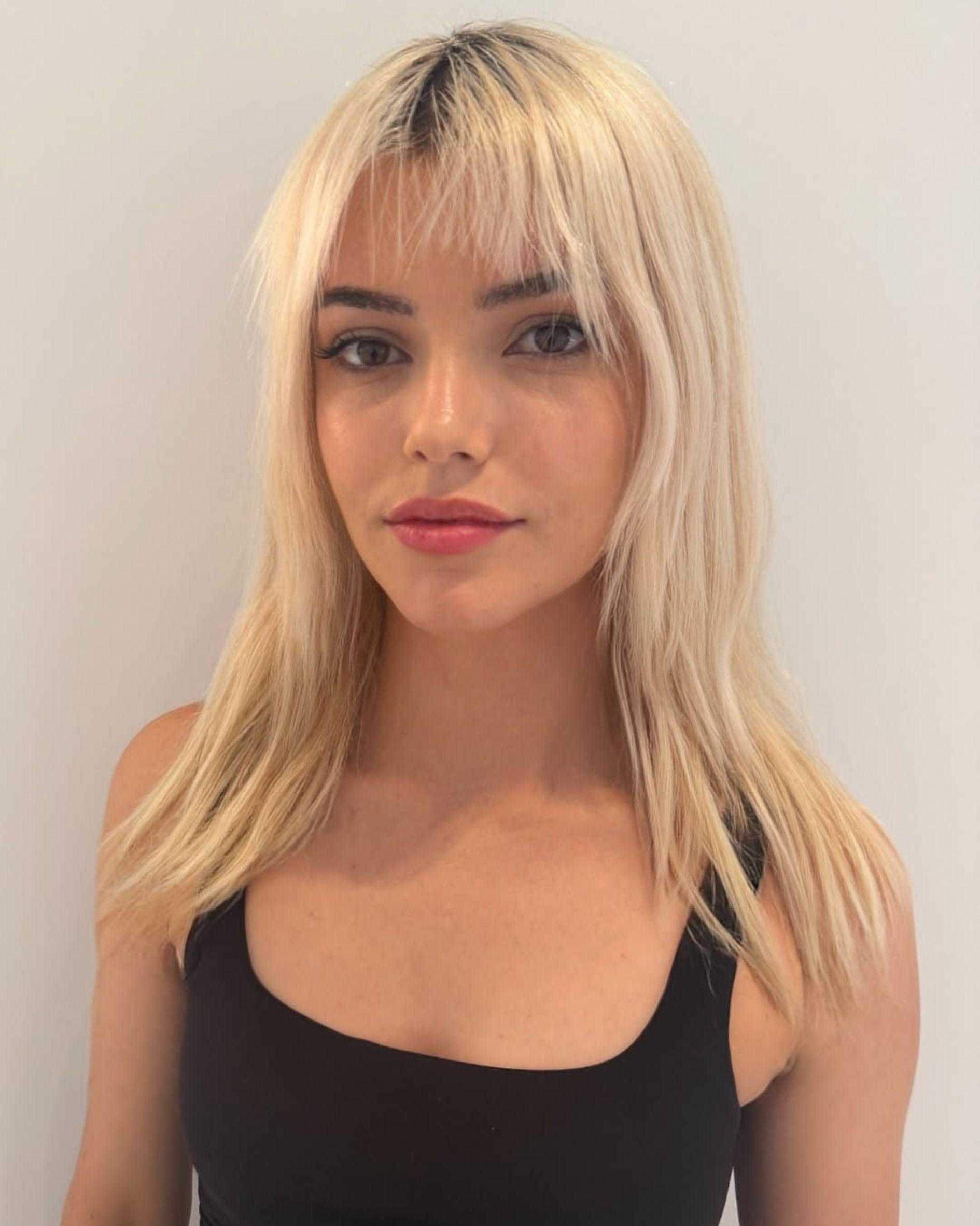 Light blonde hair with a soft shag haircut and wispy fringe, shown before a pink color transformation.