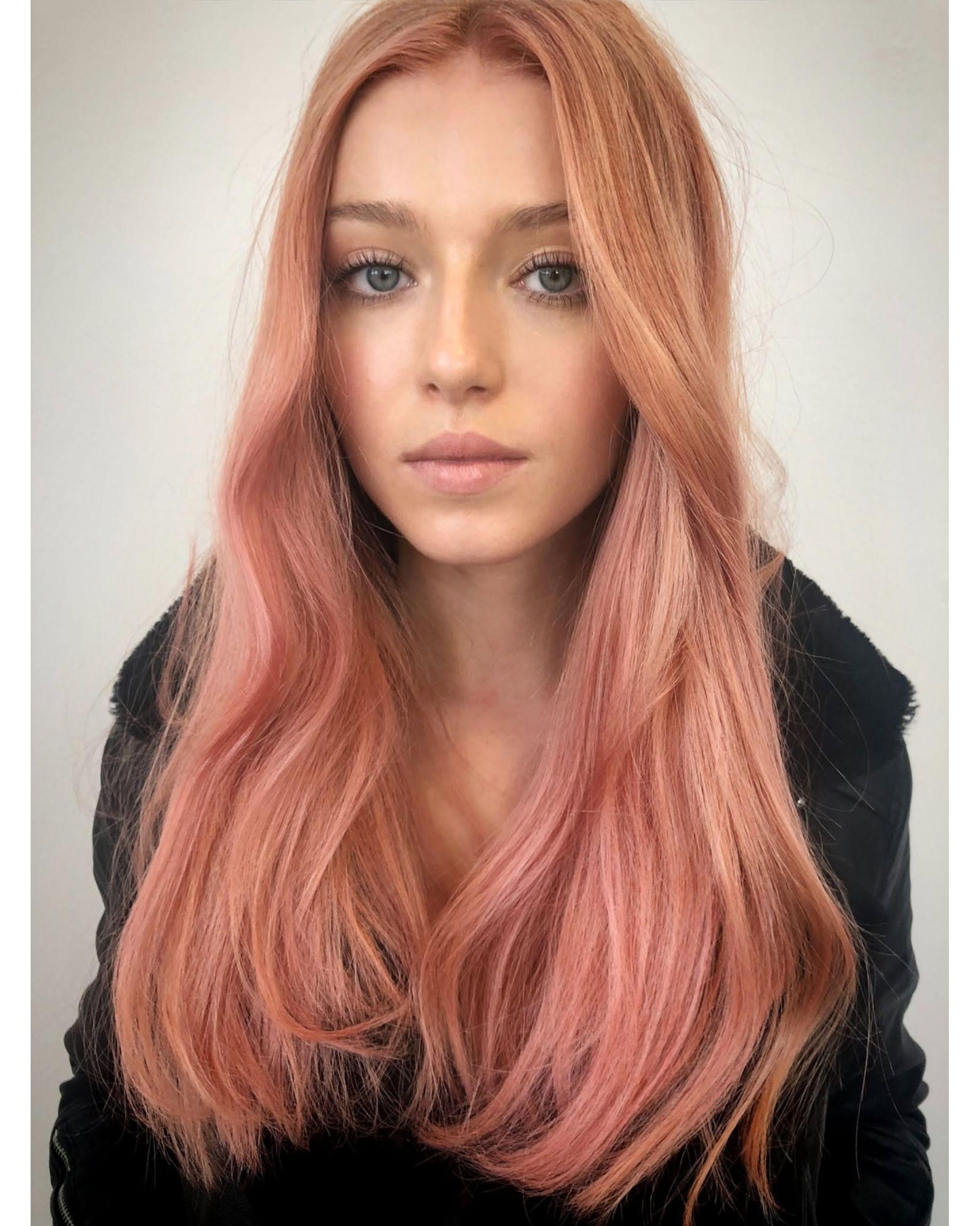 Rose gold hair color with soft dimension and shine, featuring warm peach-pink tones on long layered hair.