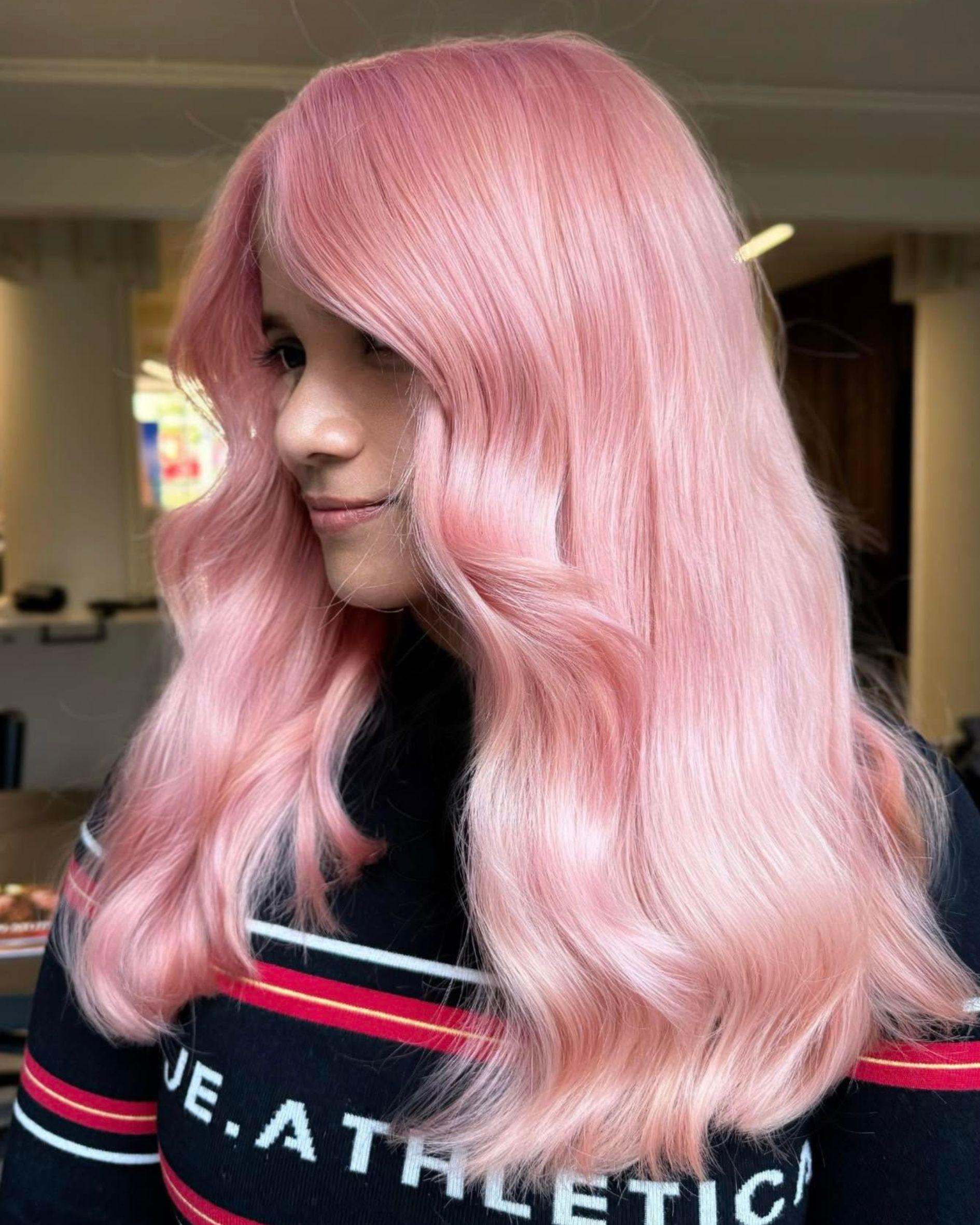 Light bubblegum pink hair with long waves and full fringe, showcasing a glossy pastel pink finish.