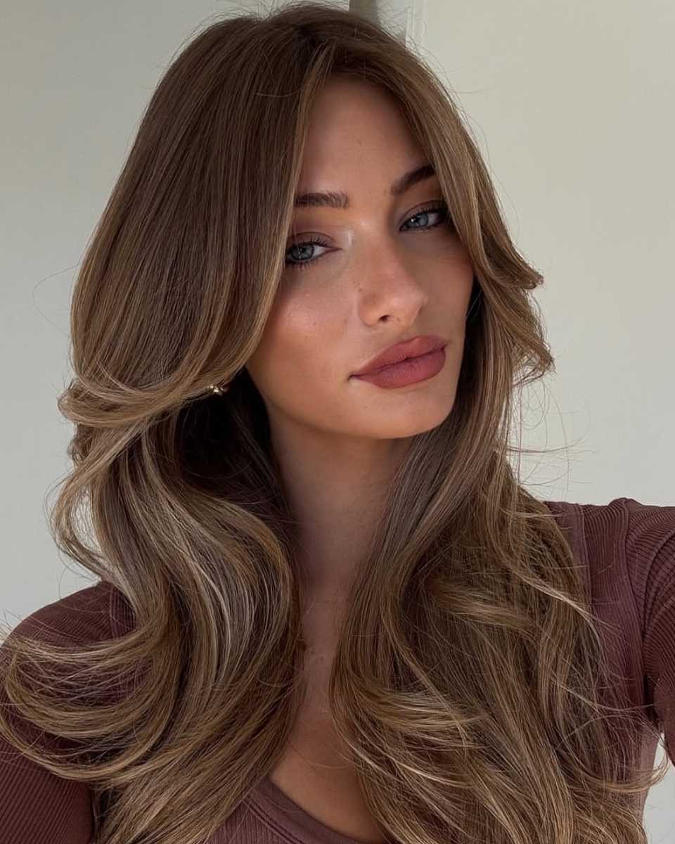 Long layered bronde hair with soft face-framing highlights and voluminous waves.