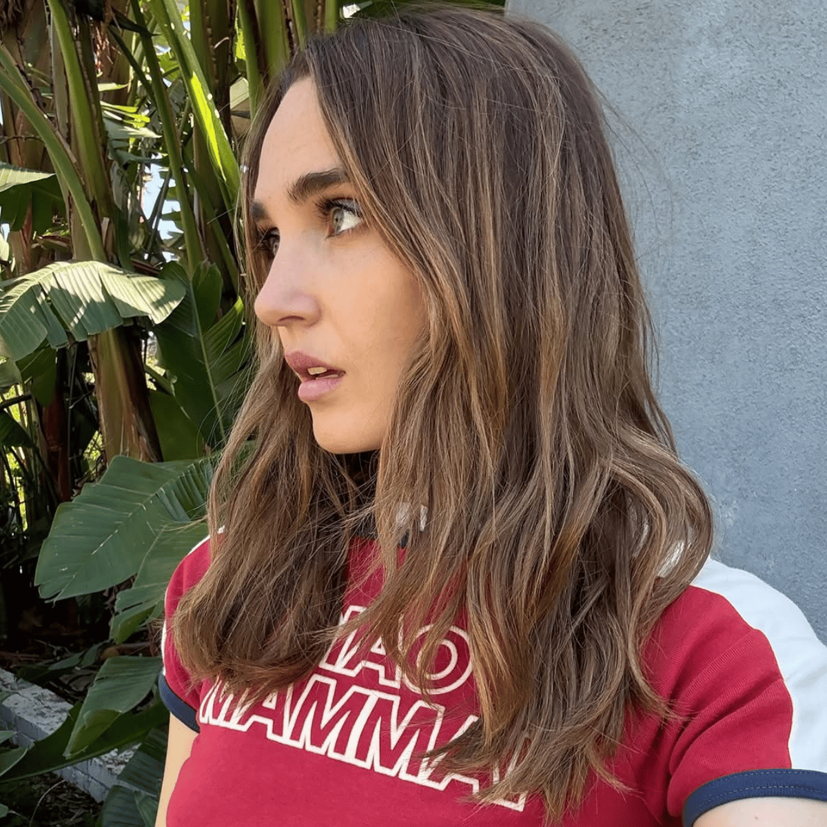 Chloe Fineman with soft, dimensional brunette hair featuring subtle highlights and a glossy finish, styled in loose waves for a natural spring look.