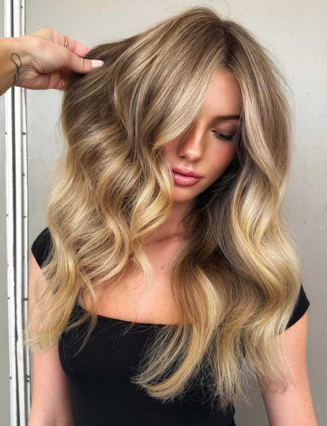 Long, luxury blonde hair featuring a soft beige-blonde balayage with bright face-framing highlights, blended shadow root and voluminous loose waves.