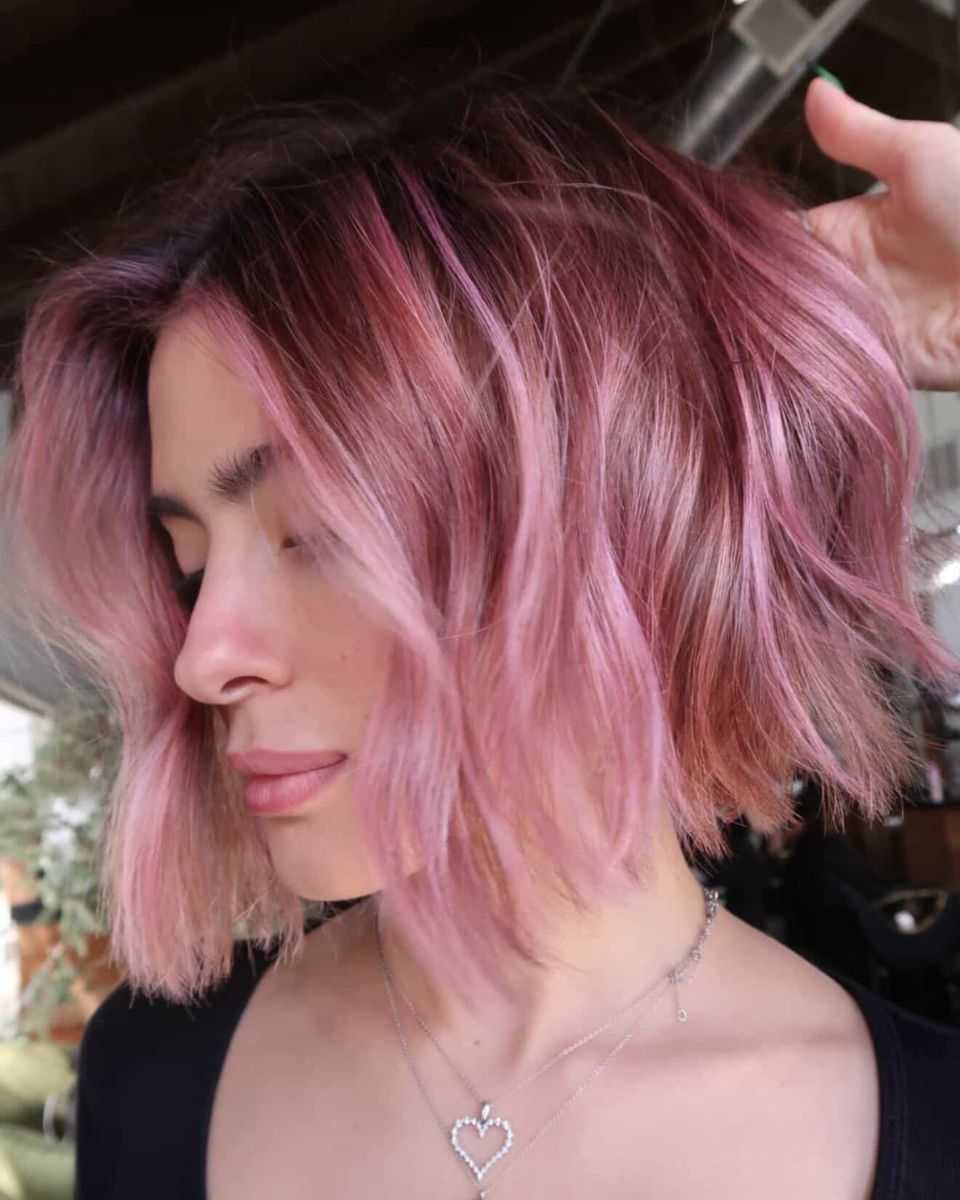 Side profile of a textured bob with a dark shadow root and soft blush-pink mids and ends, styled in loose, undone waves.