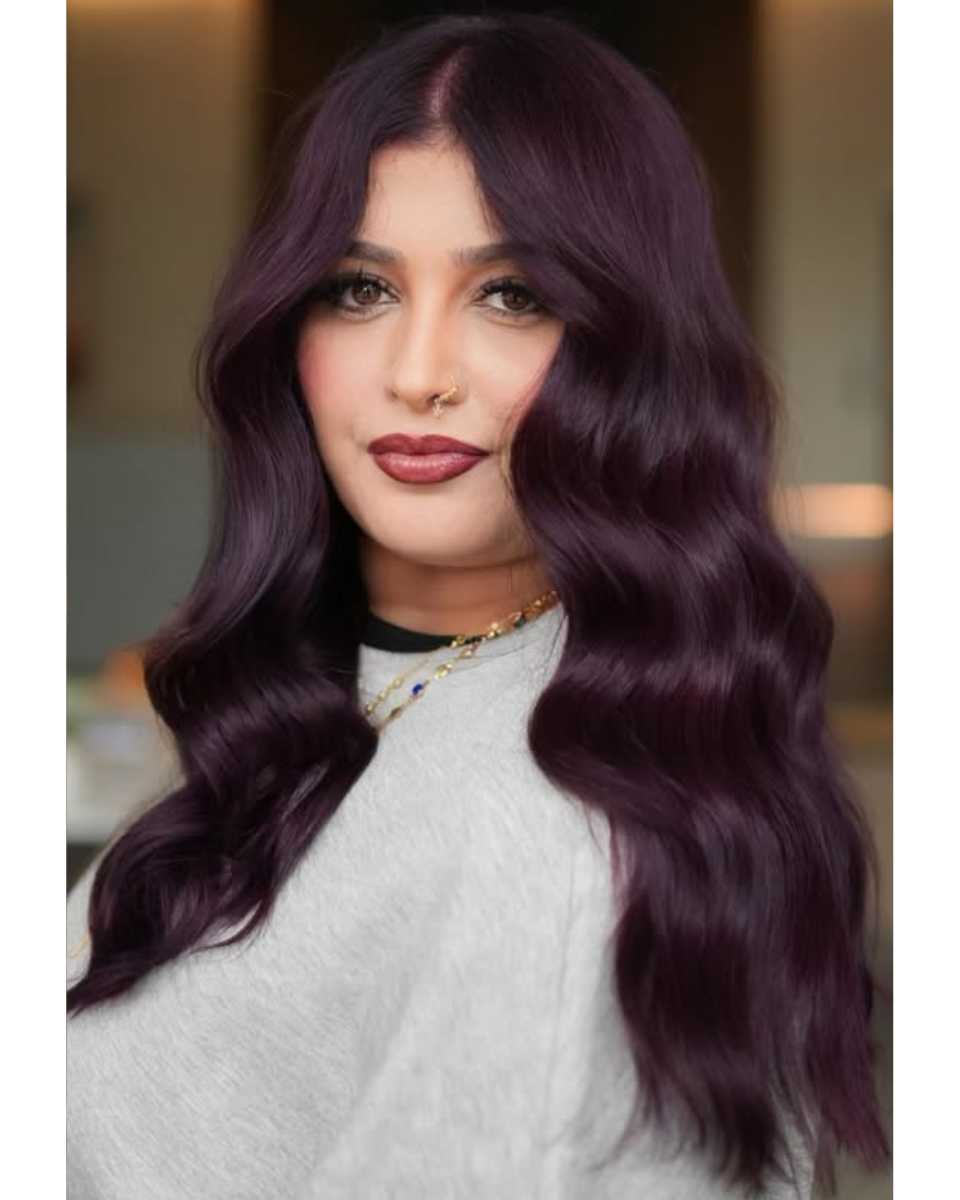 Close-up of finished long plum-purple hair color styled in soft, glossy waves with a center part.