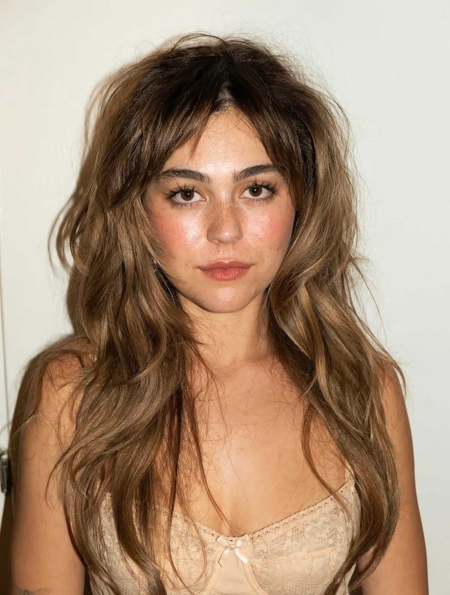 Mika Abdalla wearing a bronzed brown shag haircut with soft honey ribbon highlights, featuring textured layers, wispy fringe and dimensional brunette color.