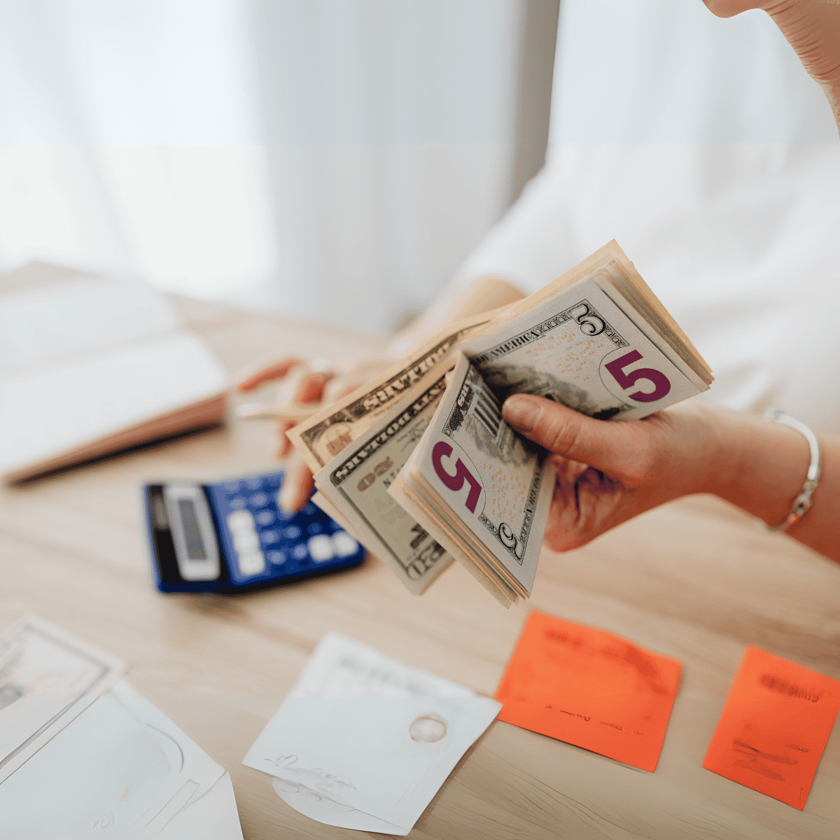 woman holding cash using a calculator at a desk
