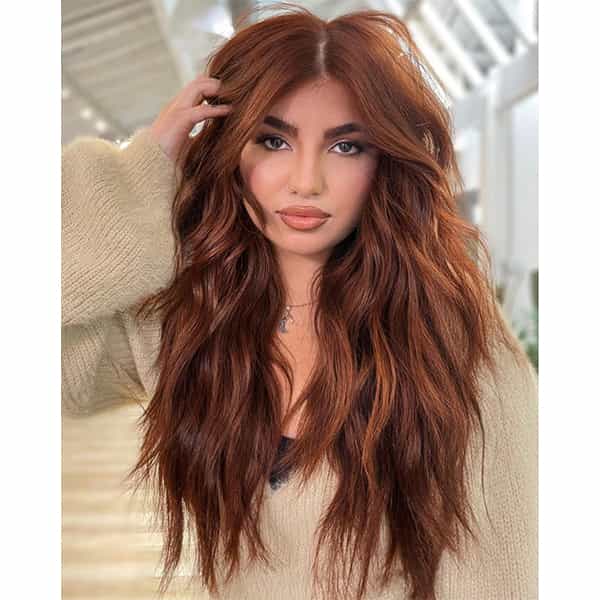 Woman with long wavy hair in trendy cowboy copper color, wearing a cozy beige sweater indoors.