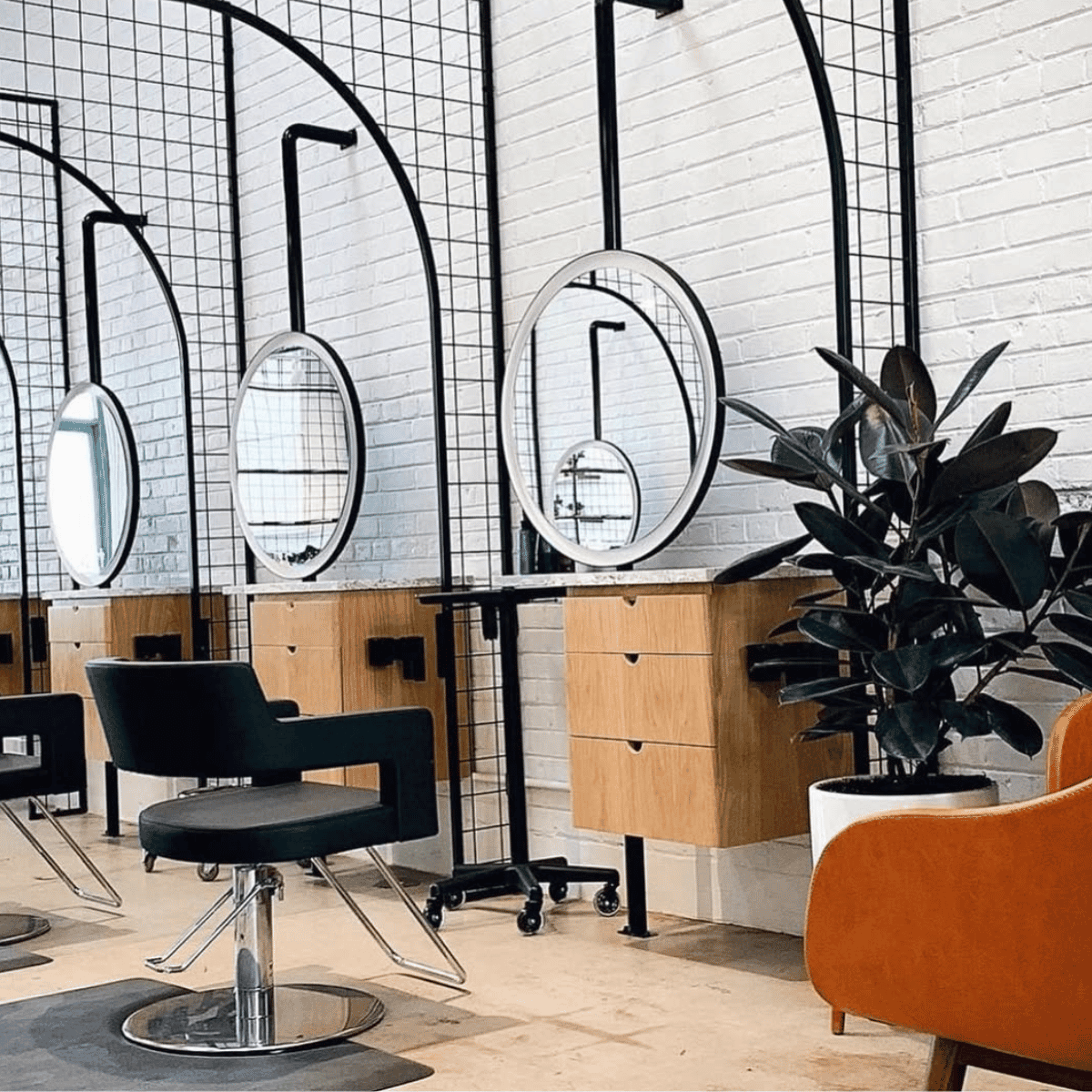 Modern salon interior with black styling chairs, lighted mirrors, and sleek white countertops under decorative pendant lighting.