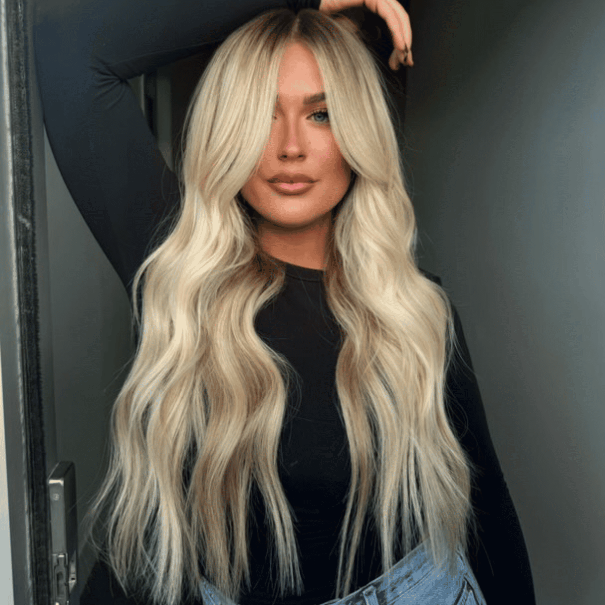 Client with long, wavy blonde Slavic extensions styled with curtain bangs and dimensional color for a seamless finish