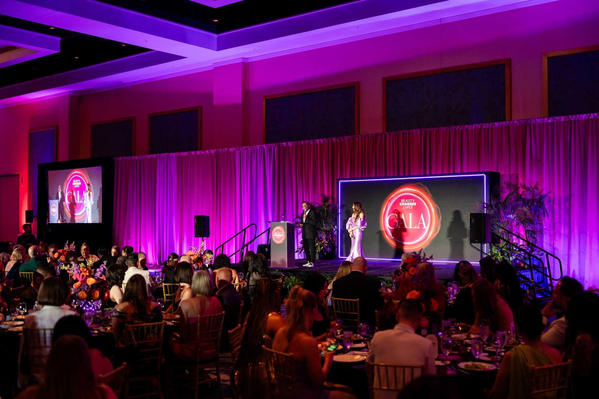 beauty changes lives 2025 gala with tables and stage with hosts sam villa and elizabeth faye addressing the crowd