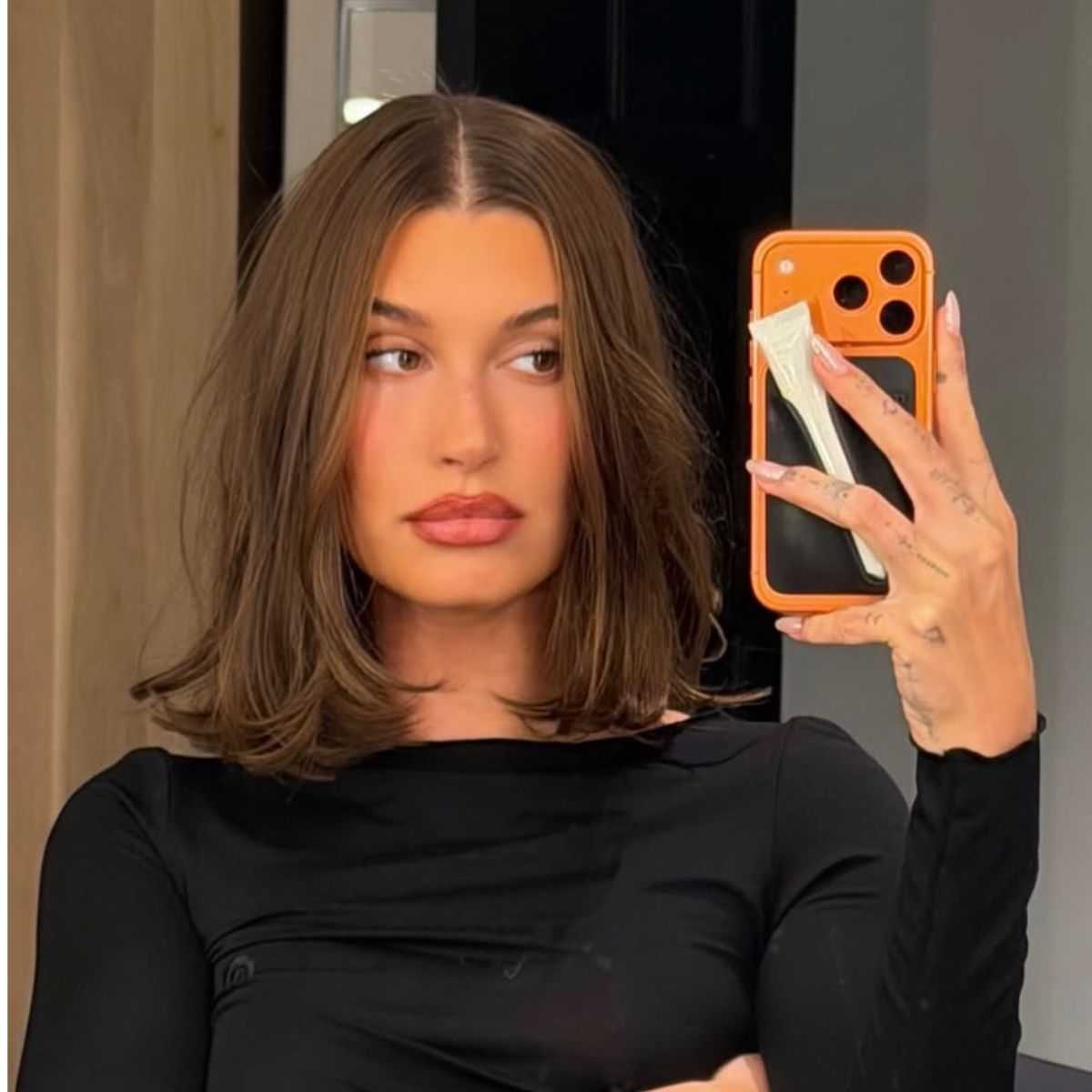 Hailey Bieber taking a mirror selfie showing a shoulder-skimming blunt lob haircut with a center part and soft face-framing layers.