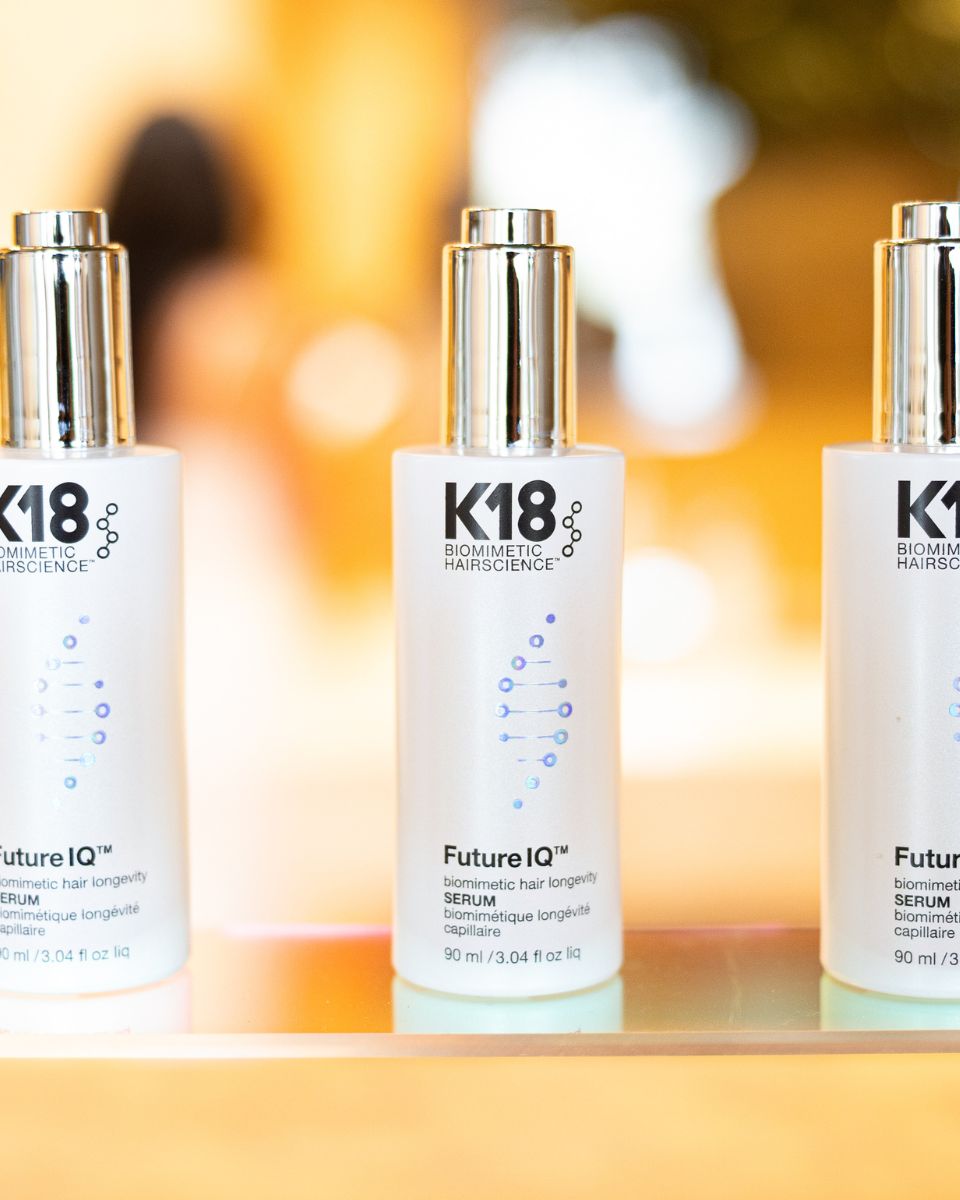 Close-up of K18 FutureIQ™ Biomimetic Hair Longevity Serum bottles displayed against a softly blurred salon background.
