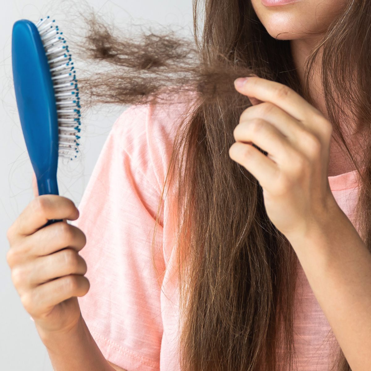 woman holding brush with hair on it shedding