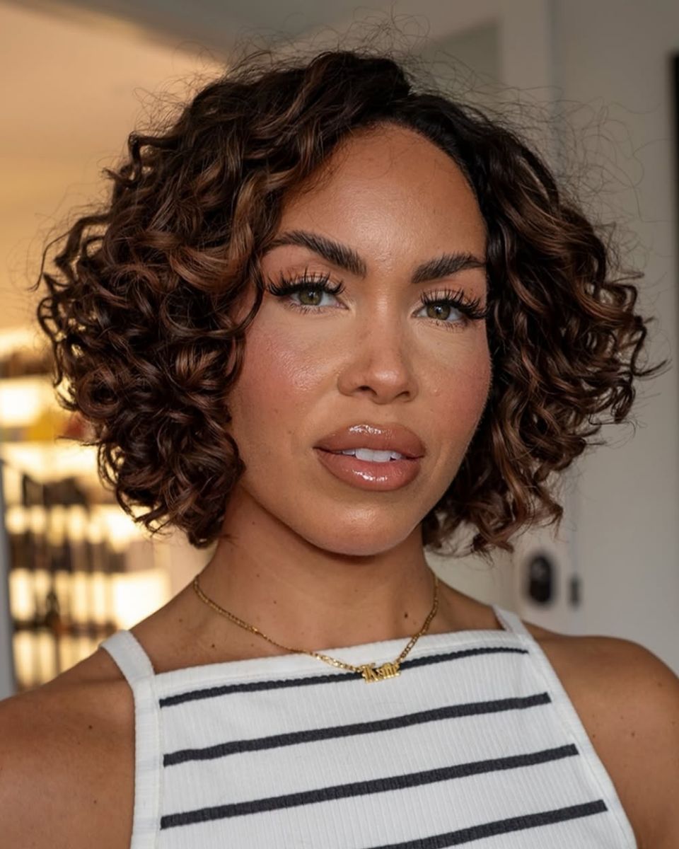 Short curly bob with soft volume and face-framing shape, a spring/summer haircut trend for defined texture.